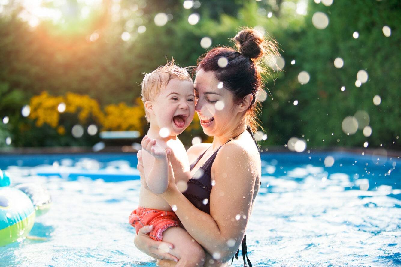 A smiling woman holding a laughing baby in a pool