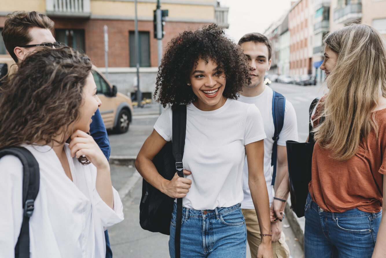 Three young women and two young men smiling and laughing outside on a street