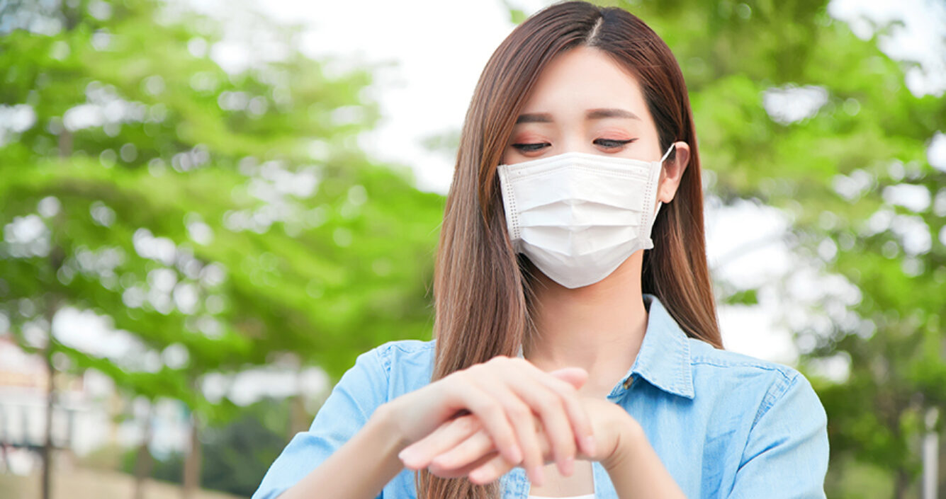 Woman rubbing hands with facemask on outside